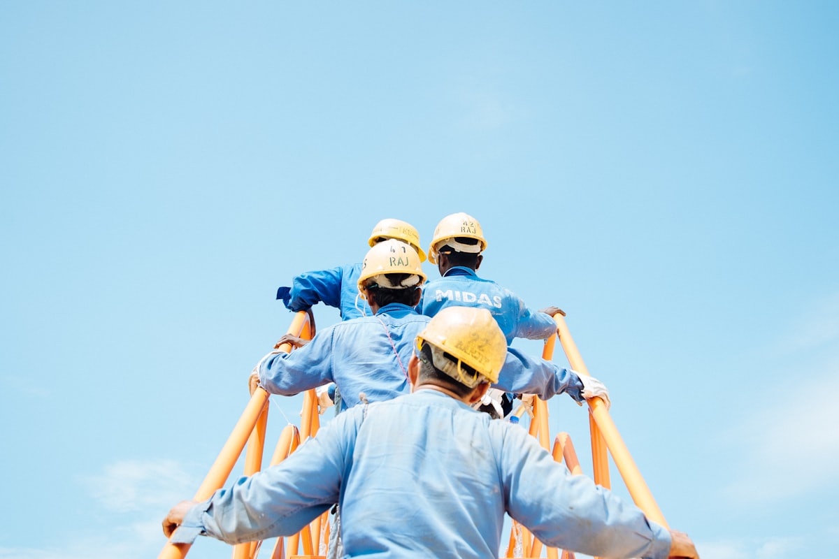 Workers in overalls and hard hats carrying a pipe together
