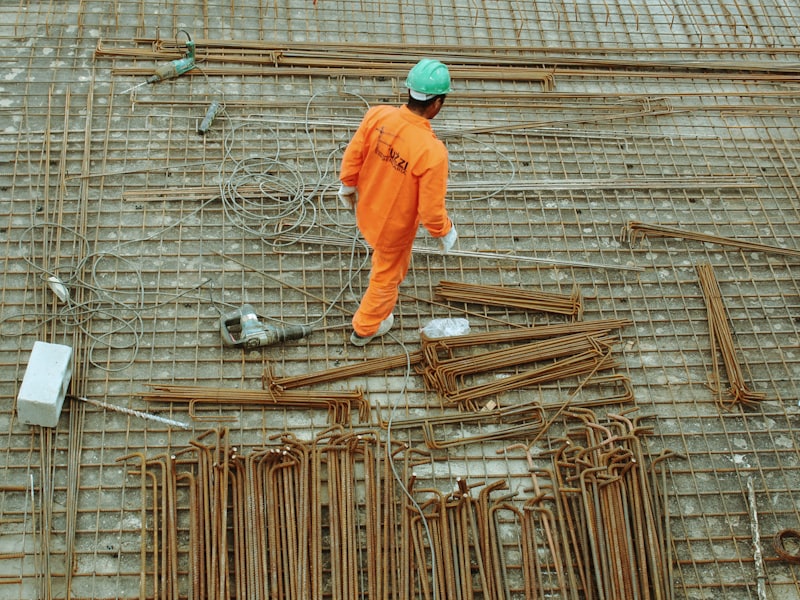 Worker in orange overalls walking across a steel reinforcement mat